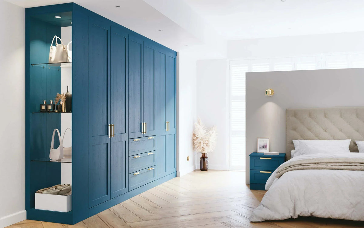 Modern blue fitted wardrobe with open shelving and gold handles in a bright bedroom