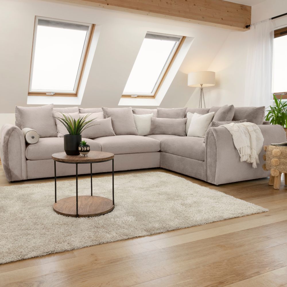 Comfortable light grey corner sofa in a bright attic living room with a wooden coffee table