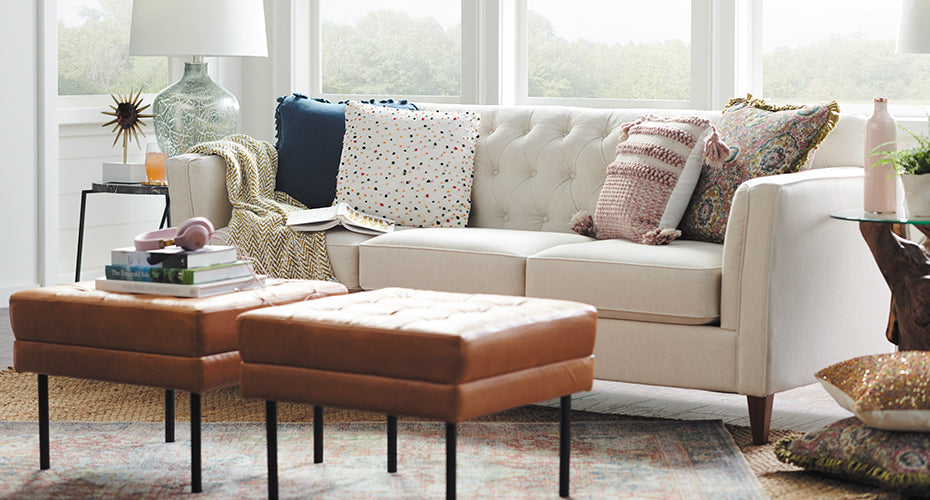 Beige tufted sofa with colorful back cushions and brown leather ottomans